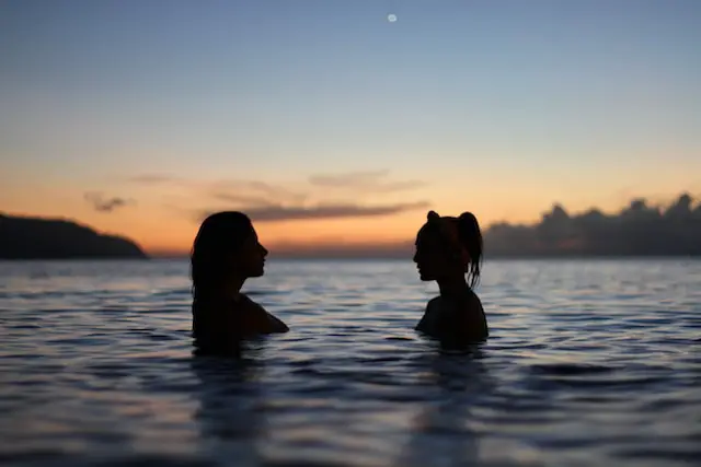 two woman standing in the lake during sunset